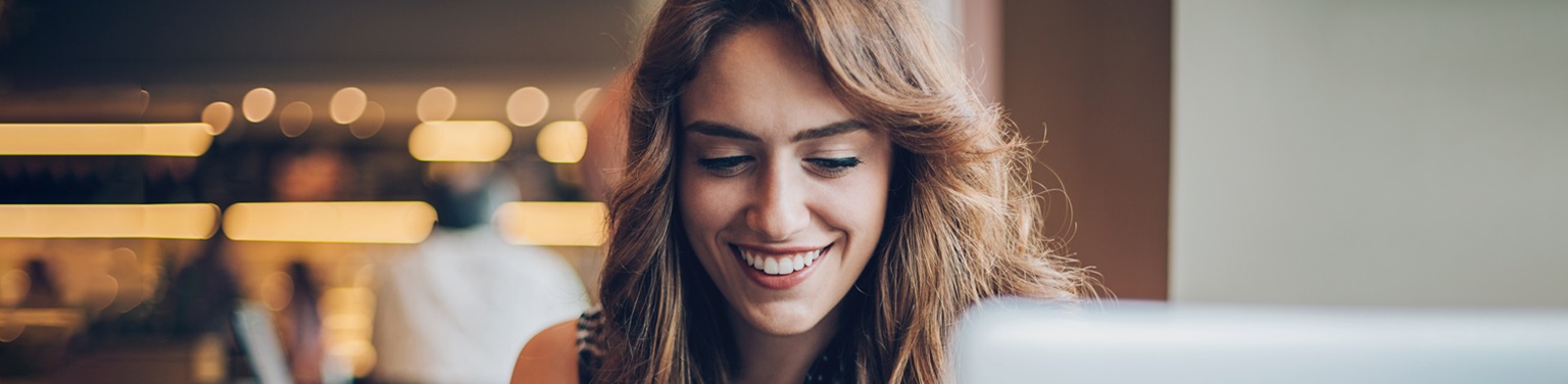 Smiling woman engaging with laptop in a collaborative workspace, reflecting innovation and community growth themes.